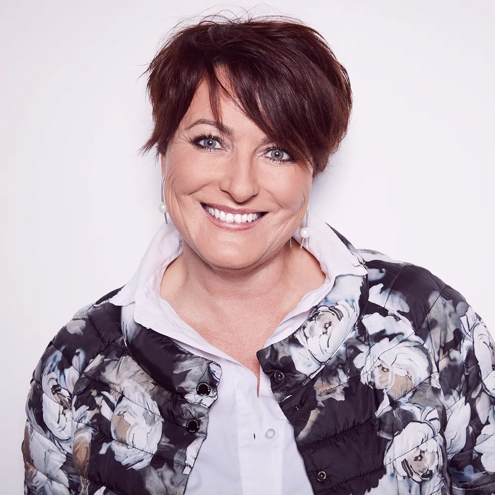 Dr. Karin Riedl, lächelnd, in weißer Bluse und geblümter Jacke
